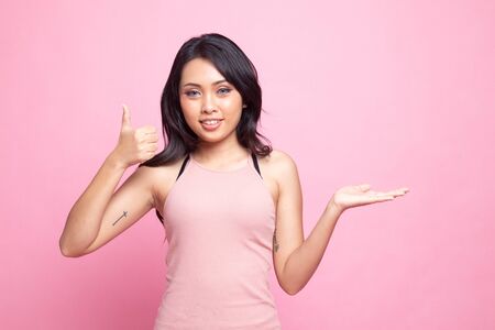 Beautiful young Asian woman show palm hand and thumbs up on pink backgroundの写真素材