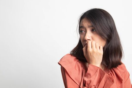 Unsure hesitant nervous young asian  woman biting her fingernails on white backgroundの写真素材