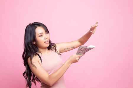 Portrait of very happy  young asian woman throwing out money banknotes on pink backgroundの写真素材
