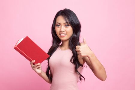 Young Asian woman thumbs up with a book on pink backgroundの写真素材