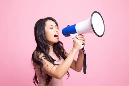 Beautiful young Asian woman announce with megaphone on pink backgroundの写真素材