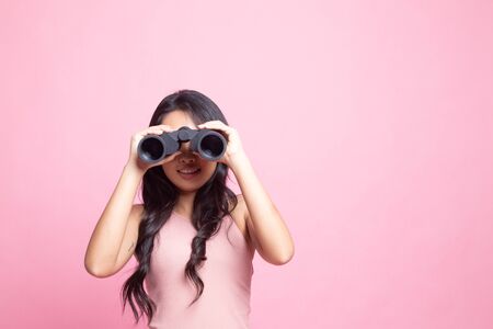 Young Asian woman with binoculars on pink backgroundの写真素材