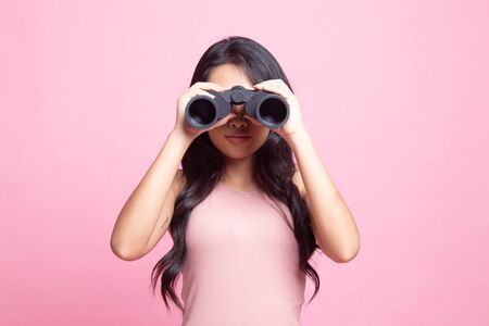 Young Asian woman with binoculars on pink backgroundの写真素材