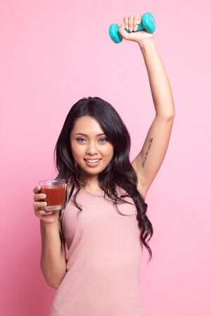 Young healthy Asian woman with dumbbell and  tomato juice on pink backgroundの写真素材