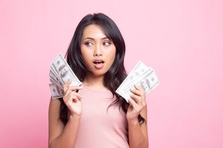 Portrait of  young asian woman  showing bunch of money banknotes on pink backgroundの写真素材