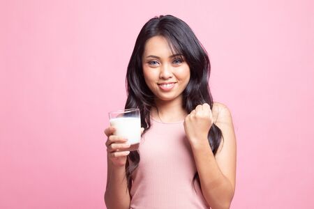 Healthy Asian woman drinking a glass of milk on pink backgroundの写真素材