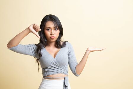 Young Asian woman show palm hand and thumbs down   on beige backgroundの写真素材