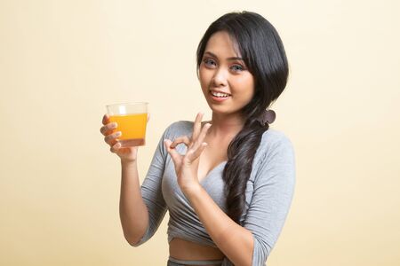 Young Asian woman show OK drink orange juice   on beige backgroundの写真素材