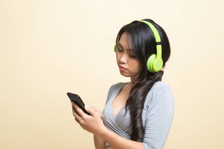 Pretty asian girl listening music with her headphones   on beige backgroundの写真素材