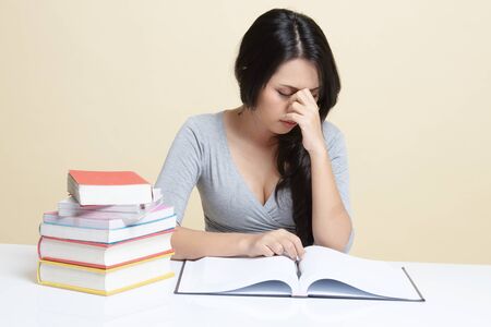 Exhausted Asian woman got headache read a book with books on table   on beige backgroundの写真素材