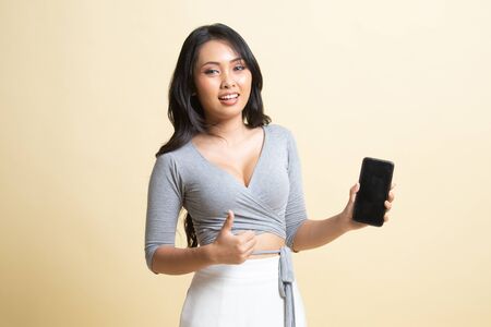 Young Asian woman show thumb up  with mobile phone   on beige backgroundの写真素材
