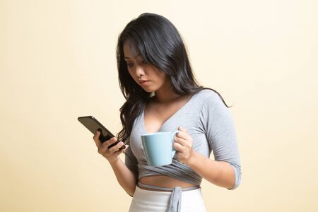 Young Asian woman with mobile phone and coffee cup   on beige backgroundの写真素材