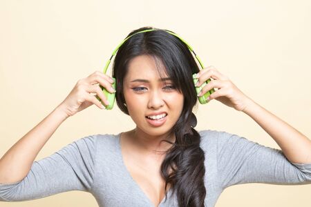 Too loud.  portrait of  young asian woman  holding  headphones and making unhappy face   on beige backgroundの写真素材