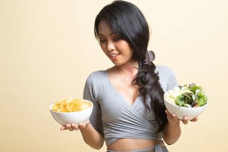 Young Asian woman with potato chips and salad   on beige backgroundの写真素材
