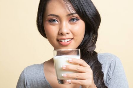 Healthy Asian woman drinking a glass of milk   on beige backgroundの写真素材