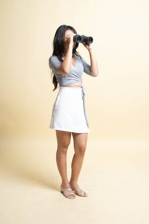 Full body of young Asian woman with binoculars   on beige backgroundの写真素材