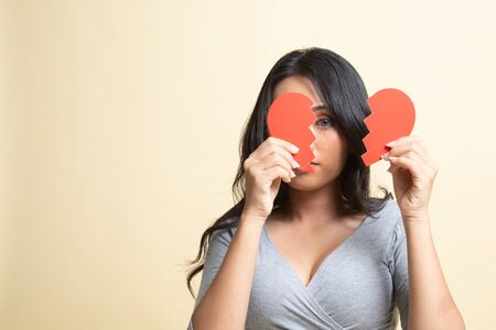 Beautiful young Asian woman with broken heart   on beige backgroundの写真素材