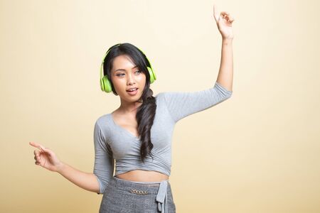 Pretty asian girl listening music with her headphones   on beige backgroundの写真素材