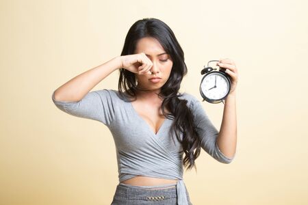 Sleepy young Asian woman with a clock in the morning   on beige backgroundの写真素材