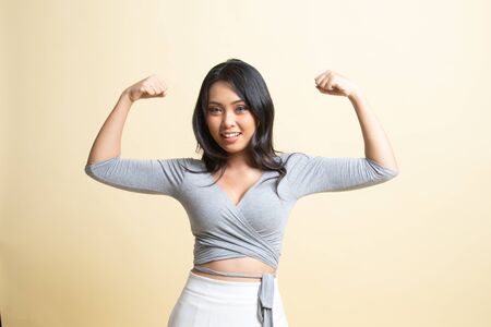 Beautiful young Asian woman flex bicep   on beige backgroundの写真素材