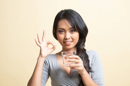 Young Asian woman show OK with a glass of drinking water   on beige backgroundの写真素材