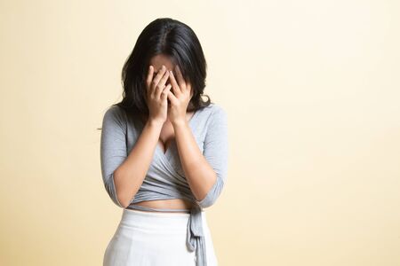 Sad young Asian woman cry with palm to face   on beige backgroundの写真素材