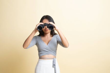 Young Asian woman with binoculars   on beige backgroundの写真素材