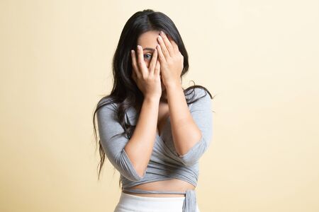 Beautiful young Asian woman peeking through fingers   on beige backgroundの写真素材