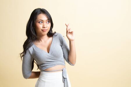 Beautiful young Asian woman cross finger   on beige backgroundの写真素材