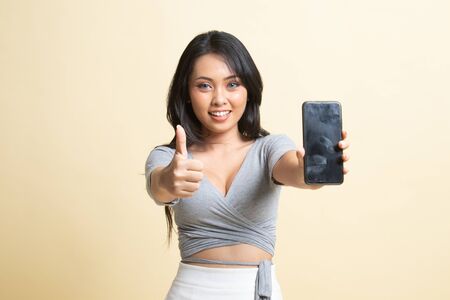 Young Asian woman show thumb up  with mobile phone   on beige backgroundの写真素材