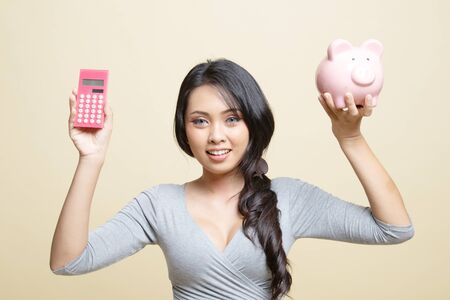 Asian woman with calculator and piggy bank   on beige backgroundの写真素材