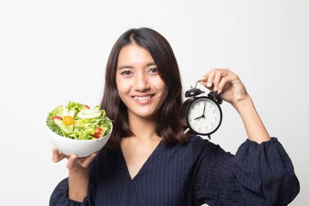 Young Asian woman with clock and salad on white backgroundの写真素材