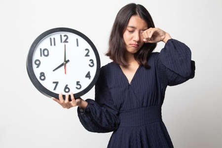 Sleepy young Asian woman with a clock in the morning on white backgroundの写真素材