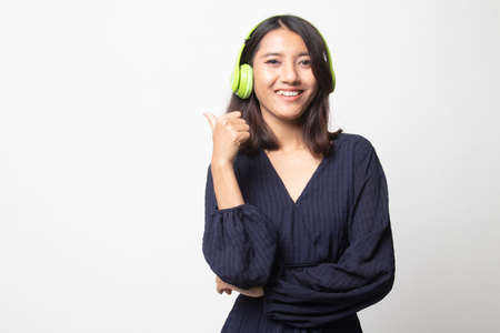 Pretty asian girl listening music with her headphones point to copy space with her thumb on white backgroundの写真素材