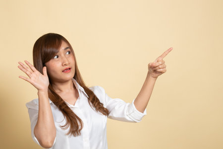 Excited Asian woman point to blank space on beige backgroundの写真素材