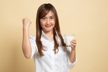 Healthy Asian woman drinking a glass of milk on beige backgroundの写真素材
