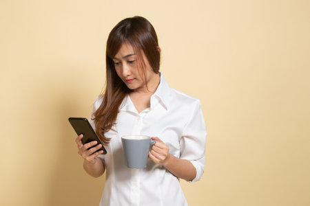 Young Asian woman with mobile phone and coffee cup on beige backgroundの写真素材