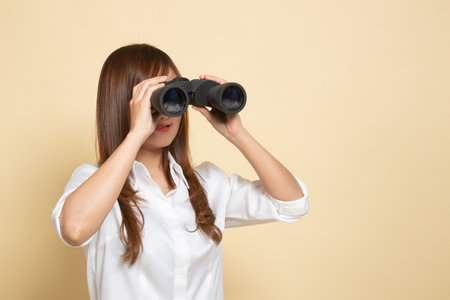 Young Asian woman with binoculars on beige backgroundの写真素材