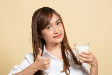 Healthy Asian woman drinking a glass of milk thumbs up on beige backgroundの写真素材