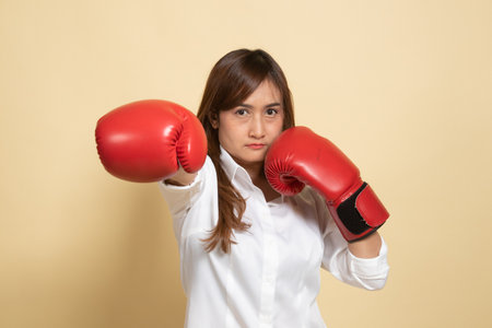 Young Asian woman with red boxing gloves on beige backgroundの写真素材