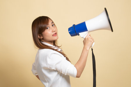 Beautiful young Asian woman announce with megaphone on beige backgroundの写真素材