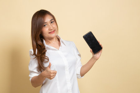 Young Asian woman show thumb up  with mobile phone on beige backgroundの写真素材