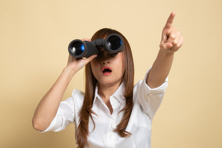 Young Asian woman  point and look with binoculars on beige backgroundの写真素材