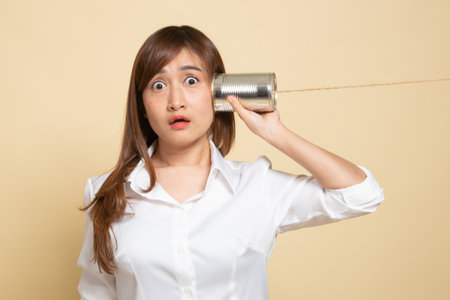 Surprised young Asian woman with tin can phone on beige backgroundの写真素材