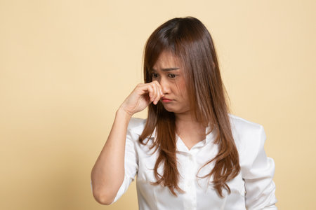 Young Asian woman  holding her nose because of a bad smell on beige backgroundの写真素材