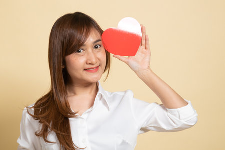 Asian woman with red heart on beige backgroundの写真素材