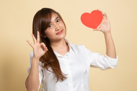 Asian woman show OK with red heart on beige backgroundの写真素材