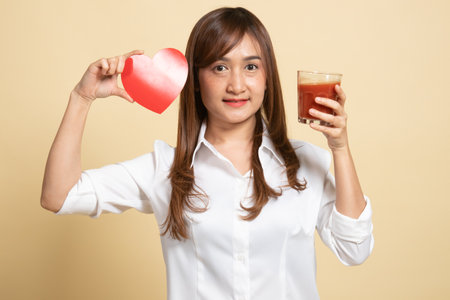 Young Asian woman with tomato juice and red heart on beige backgroundの写真素材