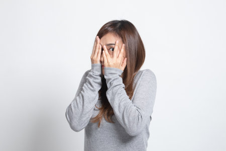 Beautiful young Asian woman peeking through fingers on white backgroundの写真素材