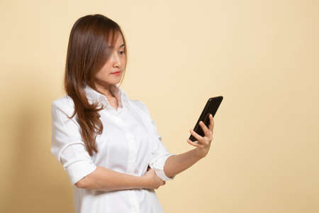 Young Asian woman with mobile phone on beige backgroundの写真素材